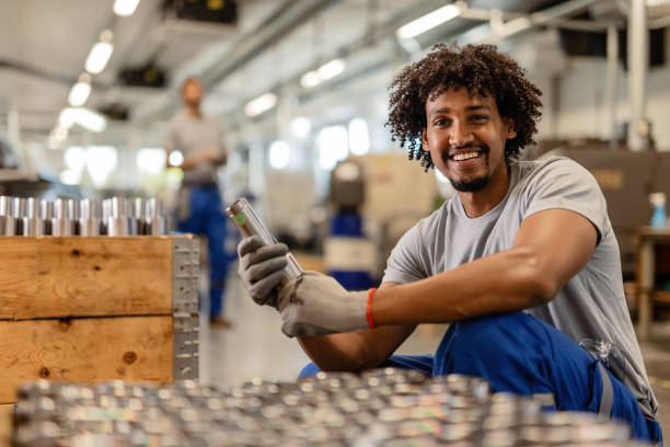 hpw Happy black steelworker inspecting finished products in a factory and looking at camera.